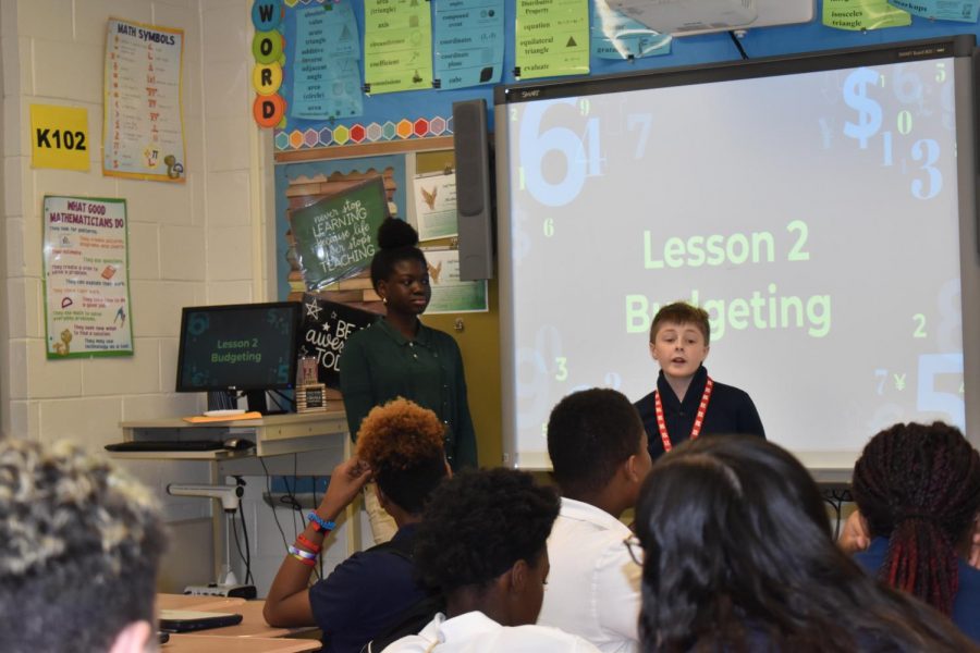 Olamide+Daodu+and+Isaac+Moran+with+their+slideshow+to+teach+seventh+graders+budgeting+basics.